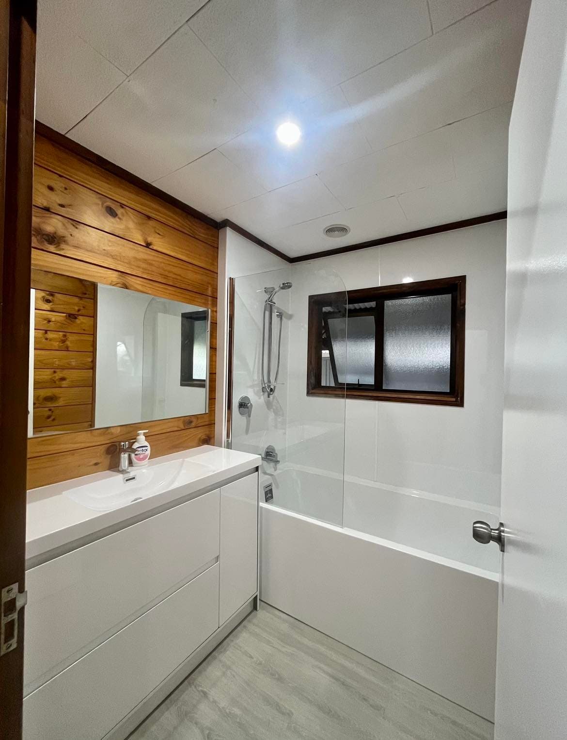 A modern bathroom with a white vanity, large mirror, and a bathtub with a glass shower partition.