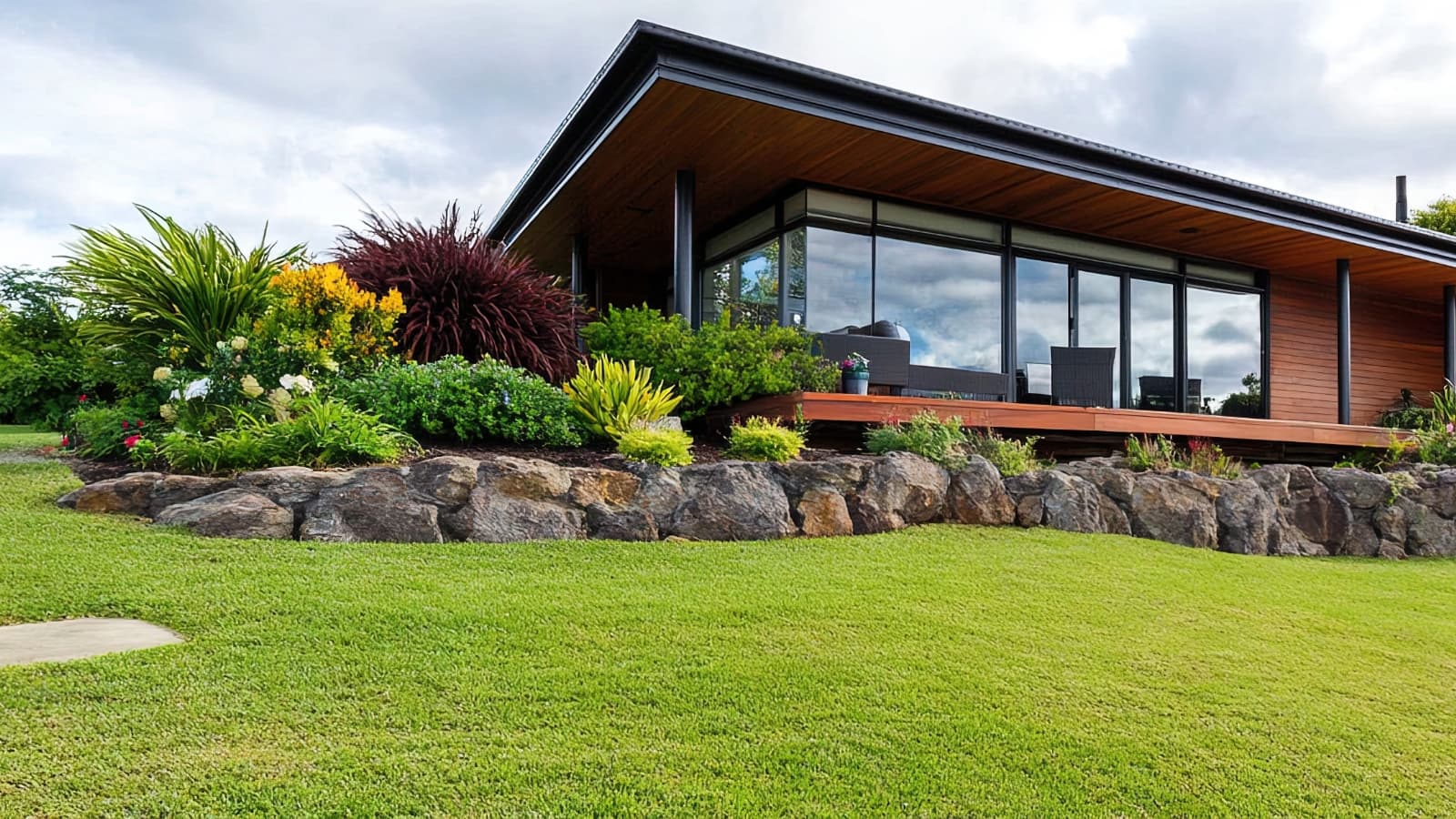 Modern home with large glass windows, surrounded by a well-maintained garden with various plants and raised stone beds.