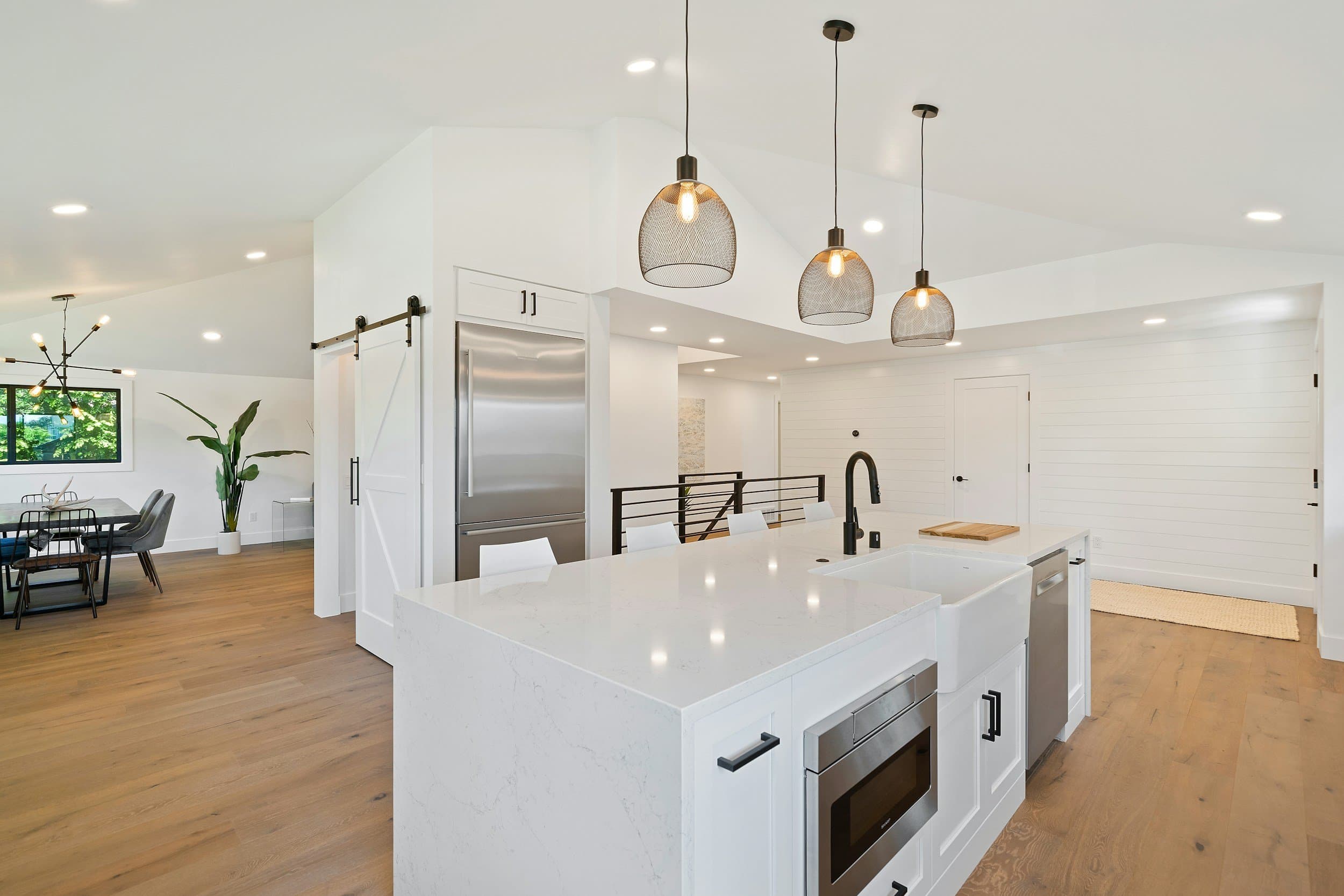 Modern open-concept kitchen with white island, black hardware, stainless steel appliances, pendant lights and dining area.